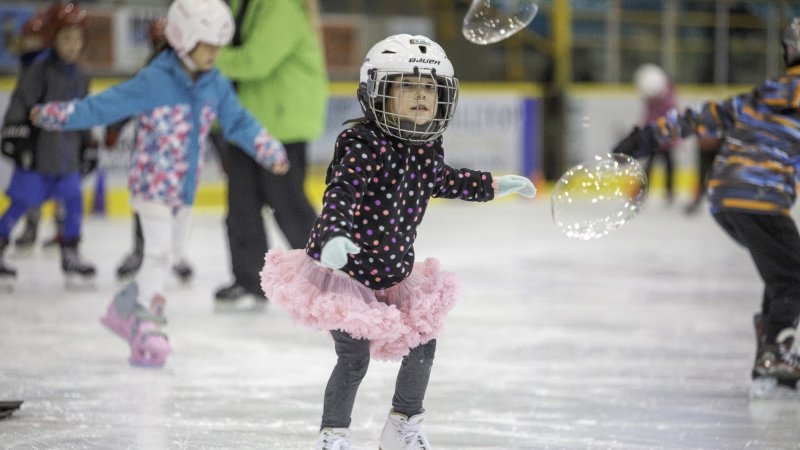 A child skating in a pink tutu with bubbles in the air.