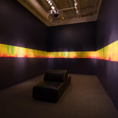 A colourful spectograph stretches across three walls of a rectangular room with a black couch in the middle.