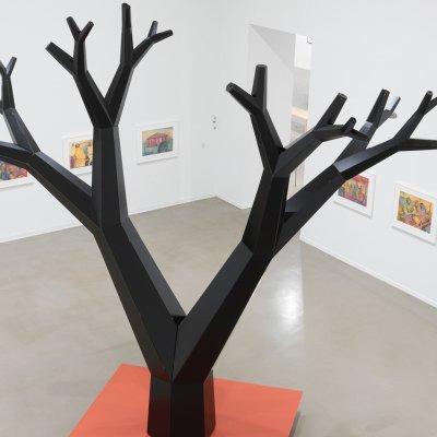 Wood and metal sculpture of a forked tree on an orange square base by Charles Campbell in a white gallery space.