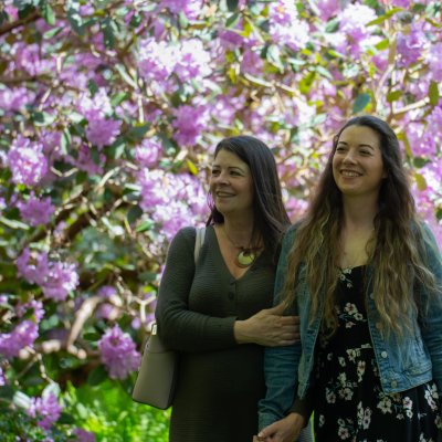 mother and daughter smiling with purple rhododendrons in the background