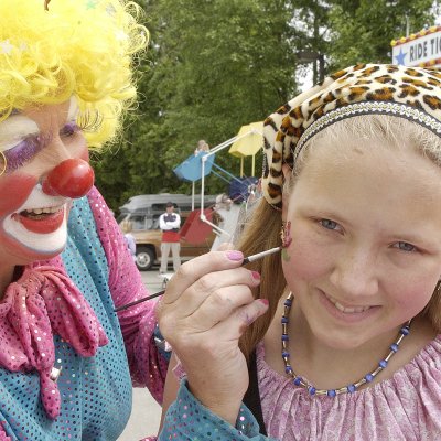 A clown painting a child's face.