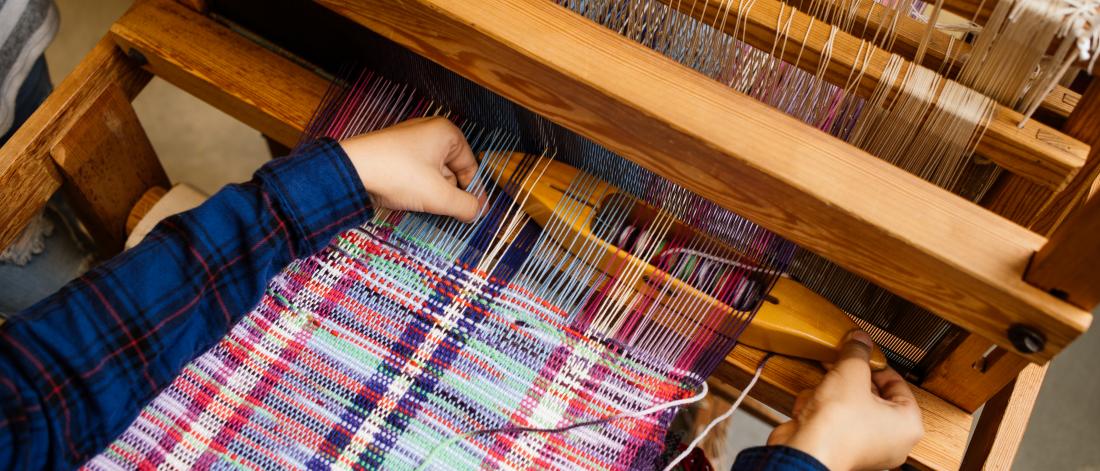 A person uses a loom with brightly coloured textile