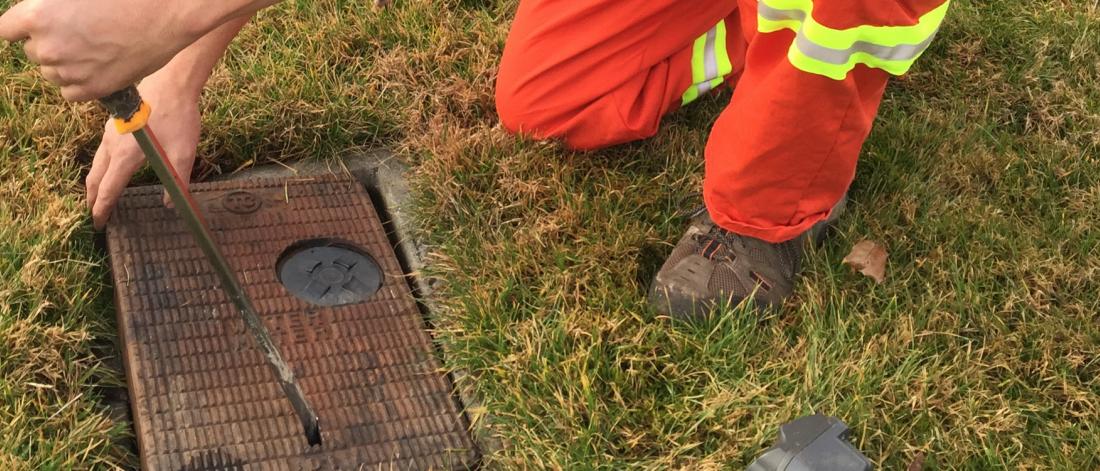 City worker removes a cover of a water meter in the grass 