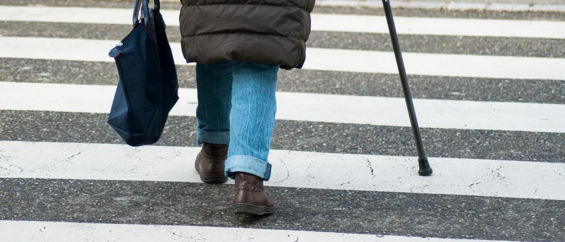 A person with a cane walks in a crosswalk