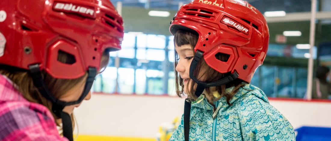 Two girls with red helmets at the ice rink