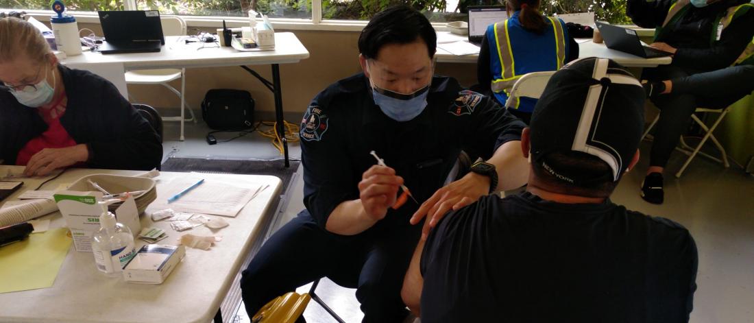 A Surrey Firefighter provides a vaccine to a man in a ball cap