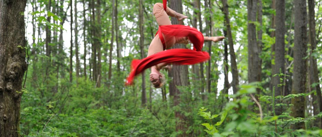 A female aerial artist in a forest and red ribbon