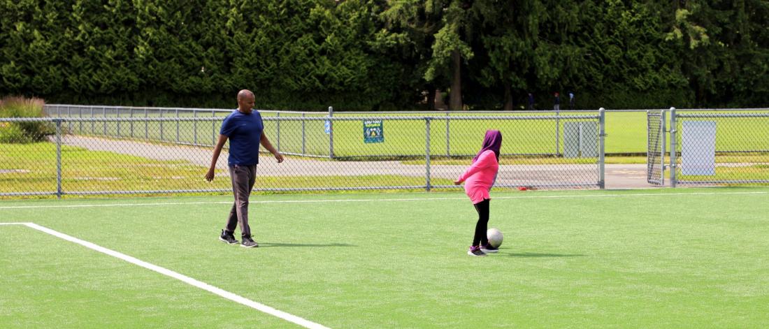 Man and child casually kick a soccer ball on a field