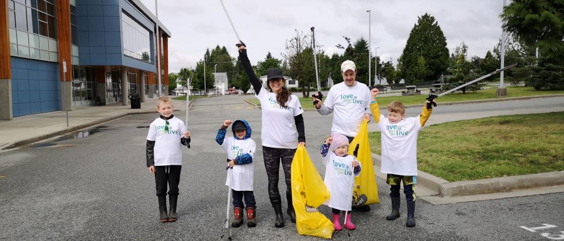 Parents and children pose with yellow litter bags and litter pickers