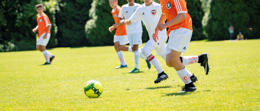 Five teenage boys play soccer on a green field