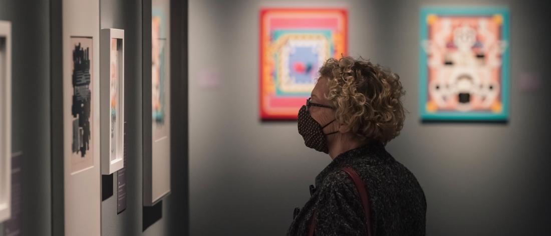 Profile image of a woman in a mask looking at artworks in a gallery.