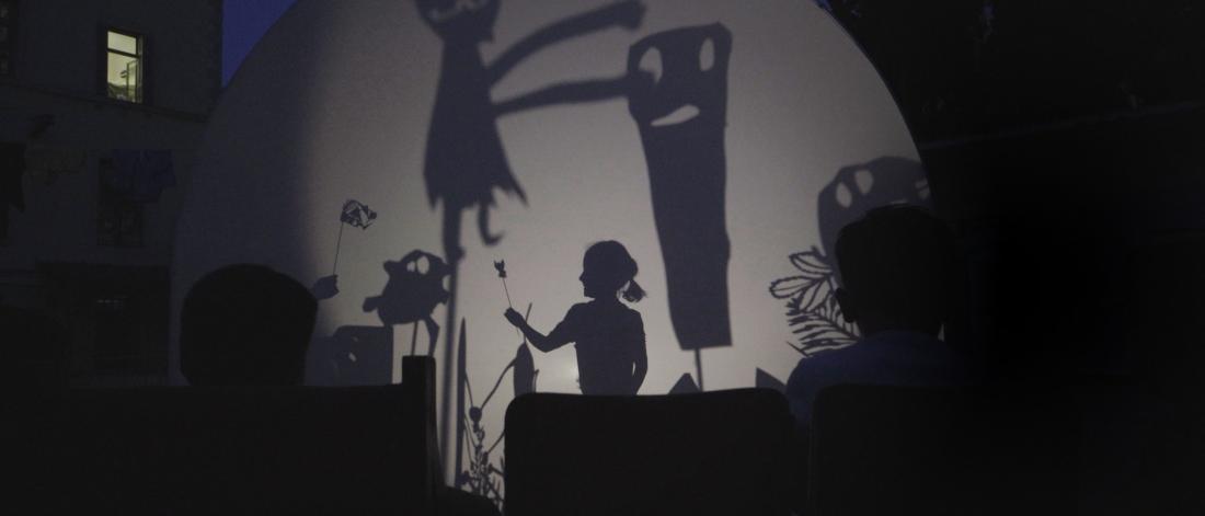 An interactive puppet show is set up outside with images projected on a tent and a child playing in the middle.