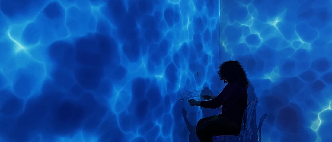 A person sits on a chair in the corner of a room whose walls look like water.