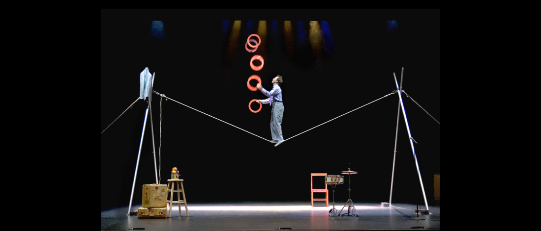 Jamie Atkins juggles red rings while standing on a tight rope