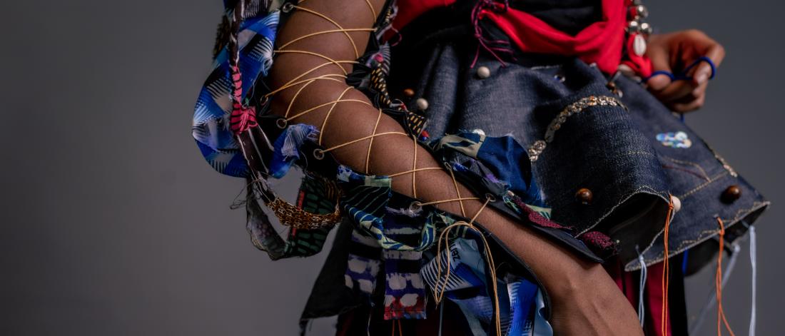 Close-up of the torso, side profile, of a Black woman dressed in a colourful outfit containing ribbons