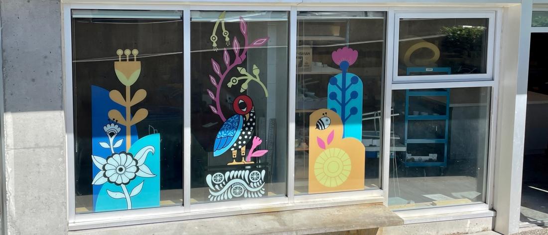 Colourful vinyl mural showing flowers and birds on window exteriors of Surrey Arts Centre classrooms.
