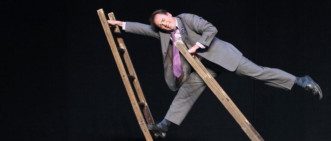 Circus performer Jamie Adkins stands on two ladders and balances between them.