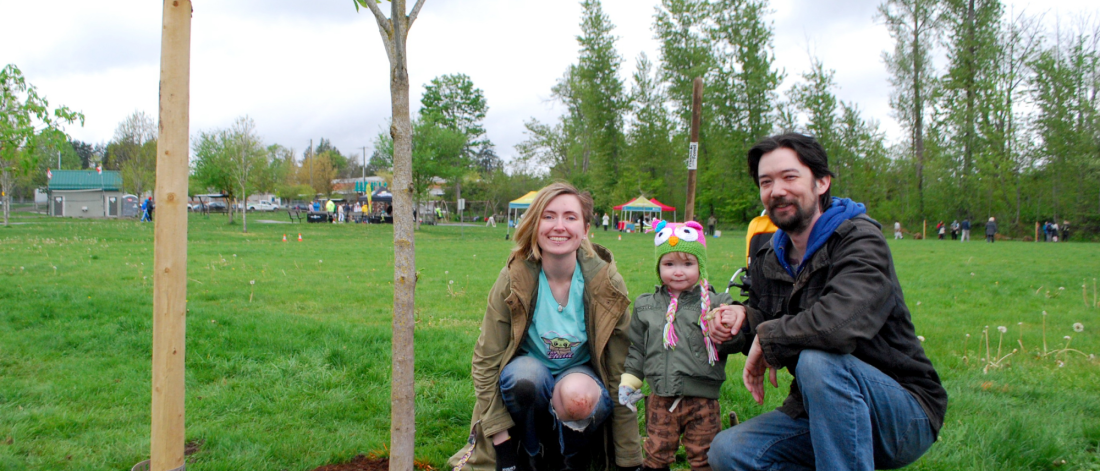 family poses beside a newly planted tree in a park