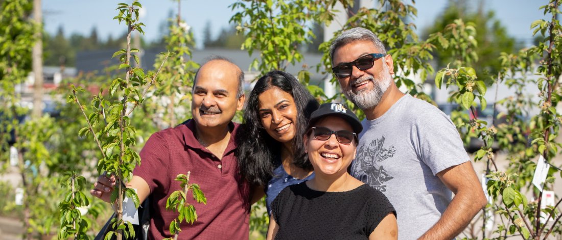 four adults smiling and standing next to a small tree