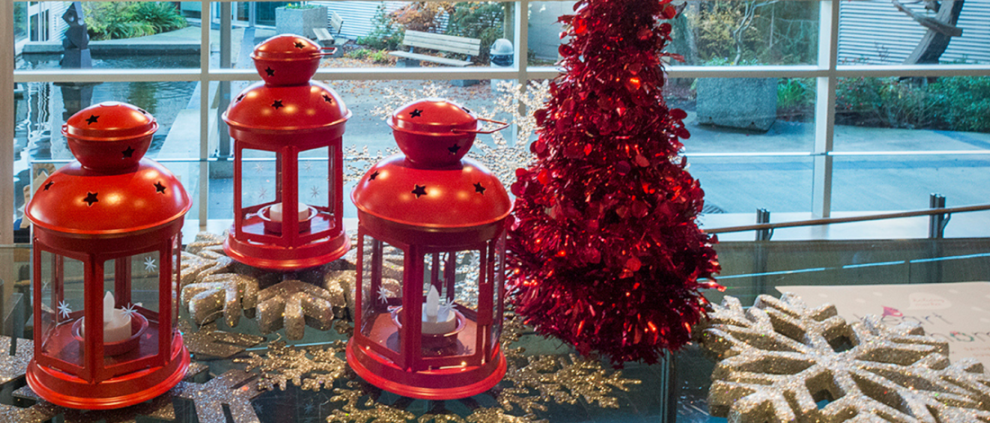 Three lanturns with tealight inside are grouped on a table with a tinsel-red Christmas tree.