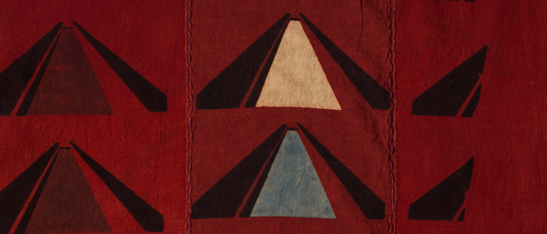 Close up of a red cotton fabric with three triangular shapes repeating in rows of two.