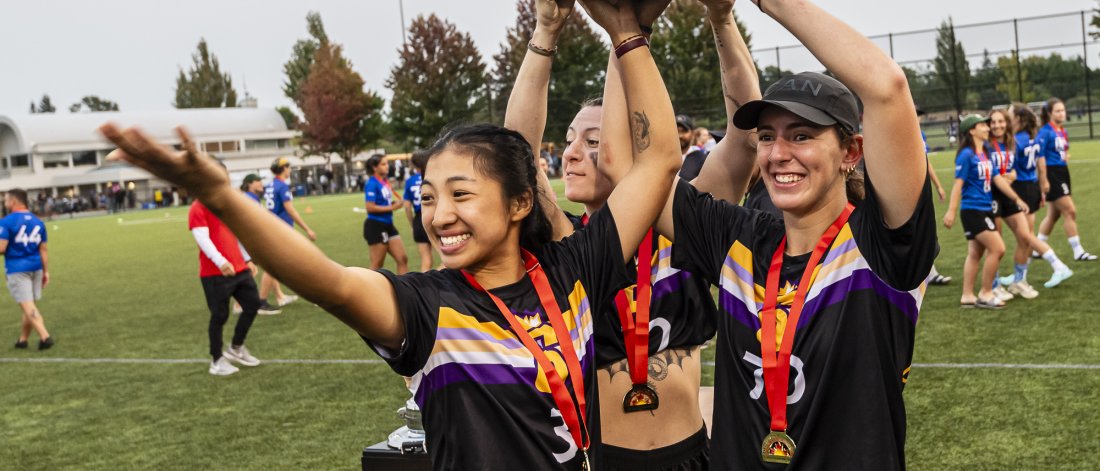 Three girls celebrating wearing medals and a holding a trophy for Ultimate Frisbee