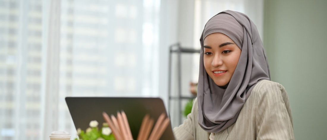 a young asian woman in a grey hair covering at a computer