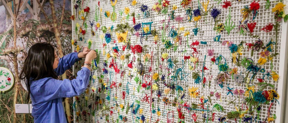  A person is attaching colorful flowers to a mesh grid as part of an interactive art installation.