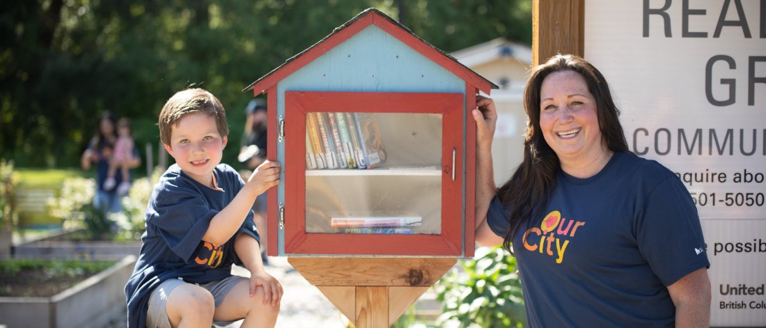 a woman and child pose beside a mini library box
