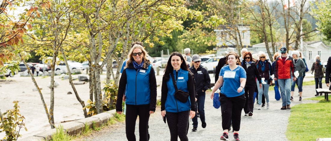 A group of people wearing matching blue vests walks along a park path.