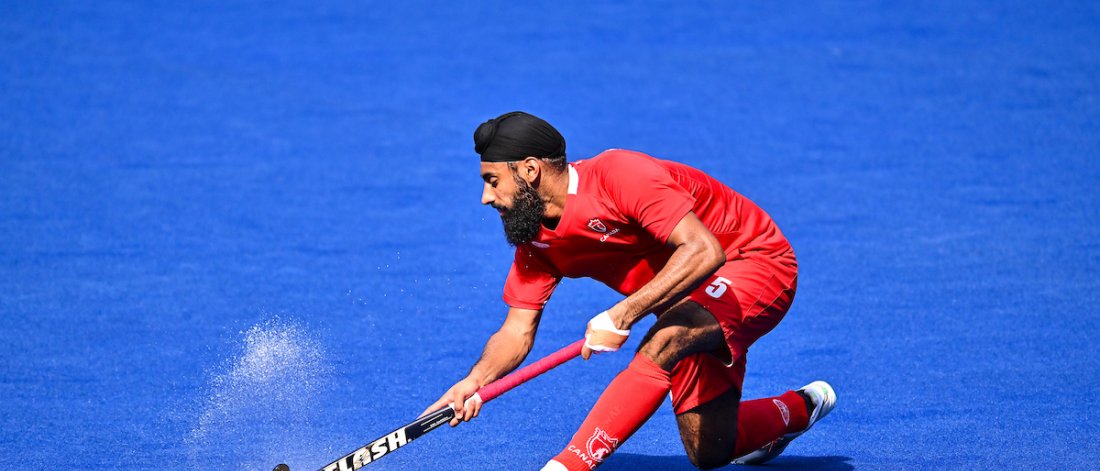  A field hockey player in action, dressed in a red uniform, skillfully controlling the ball on a bright blue turf. A field hockey player in action, dressed in a red uniform, skillfully controlling the ball on a bright blue turf.