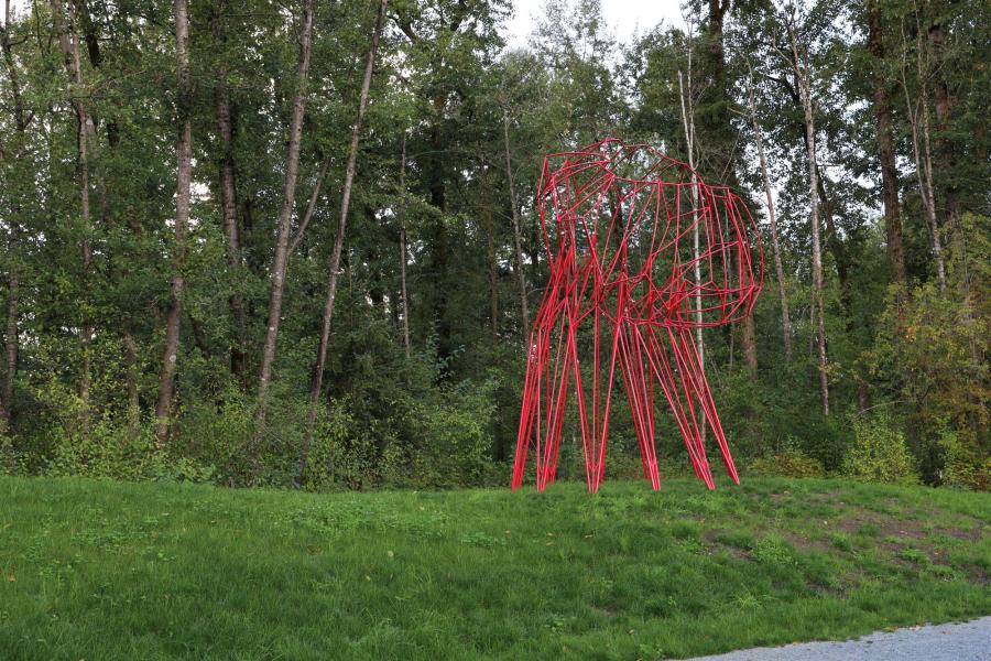 A large red metal sculpture in a wooded greenspace 