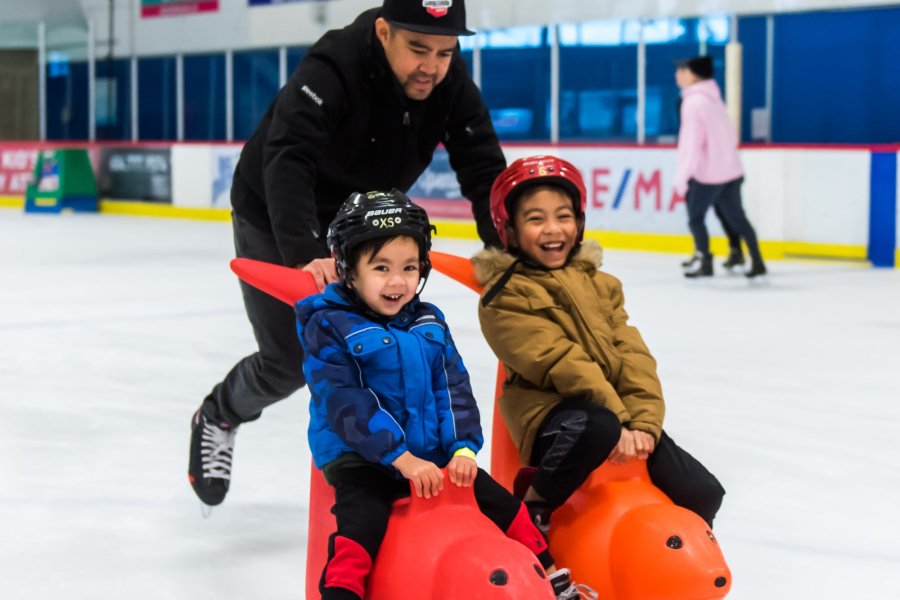 Two kids laughing ice skating with their parent.
