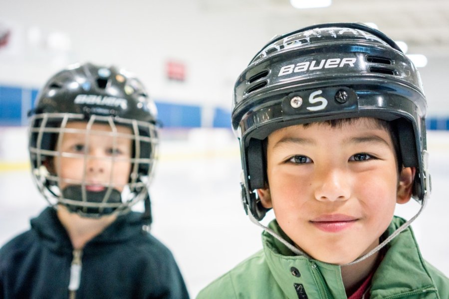 Two kids smiling with hockey helmets on.