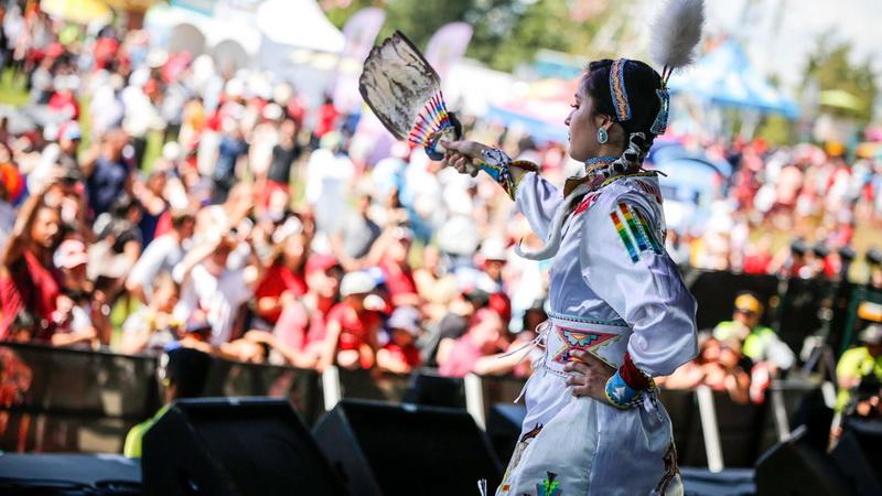 An Indigenous woman performs on stage outdoors