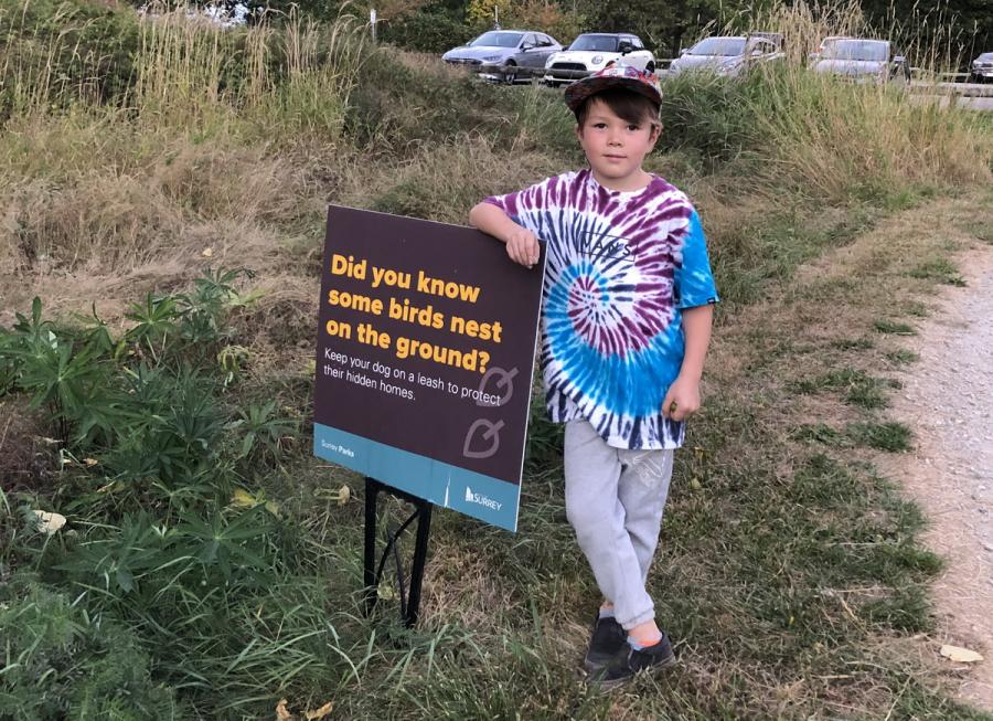 A young boy stands next to signage in a park