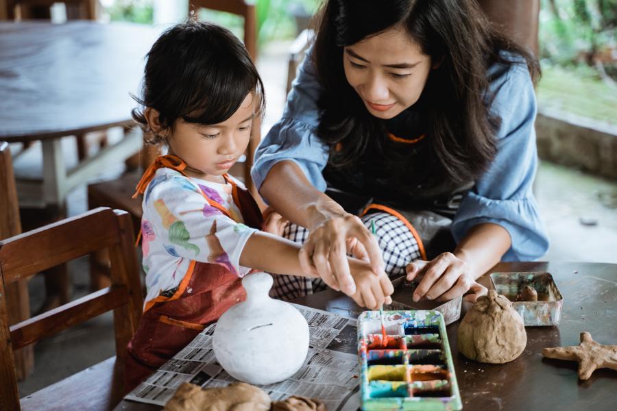 Child painting a pottery piece with mom