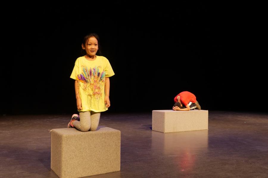 Two children standing on blocks on a black stage