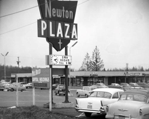 A black and white photo of a strip mall and sign that says Newton Plaza