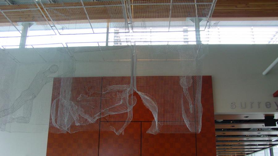Four bodies made of wire mesh are in different positions amidst a block of mesh hanging from a ceiling