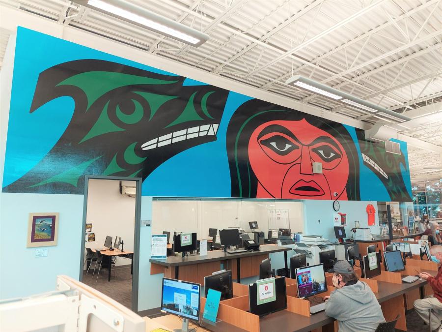 A mural inside a library above computers. An Indigenous man and two green wolves