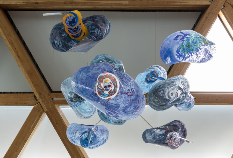 Image of a hanging sculpture made from acetate sheets rolled into cones and hung in spirals, painted in shades of blue with words stenciled on. Photo from underneath the sculpture looking straight up at it.