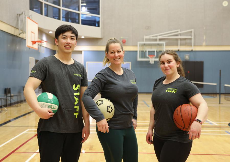 Recreation staff holding sports equipment in the gym.