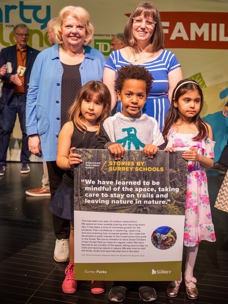 A teacher and three children holding a poster, standing on a stage with Mayor Brenda Locke