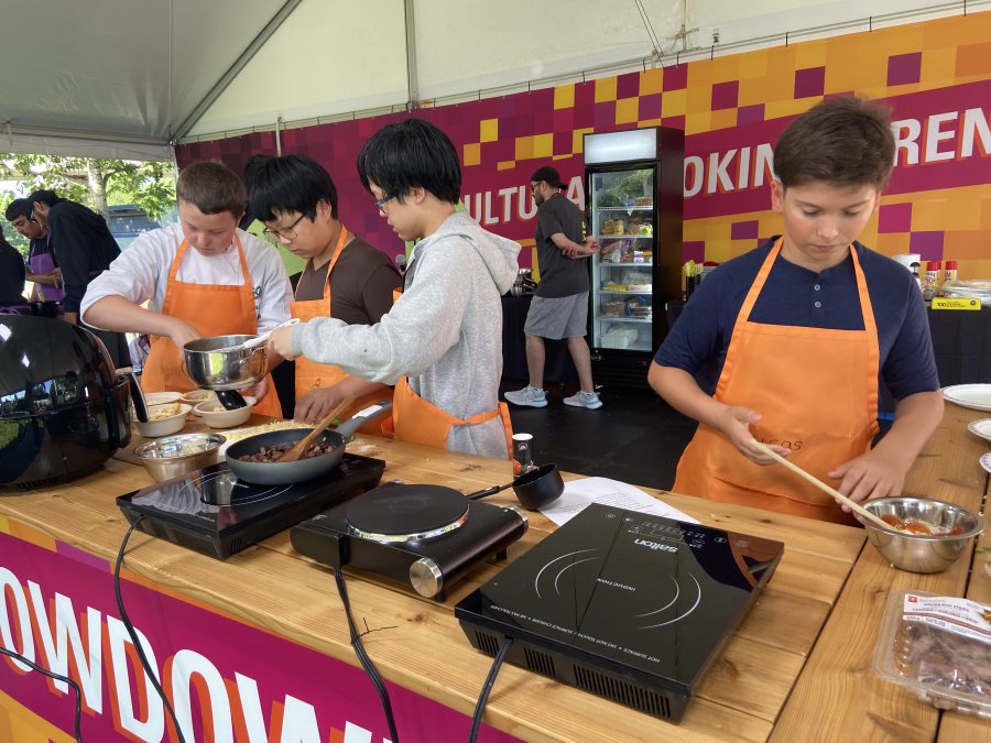 Four youth are working together at to make a food dish over three hotplates. 