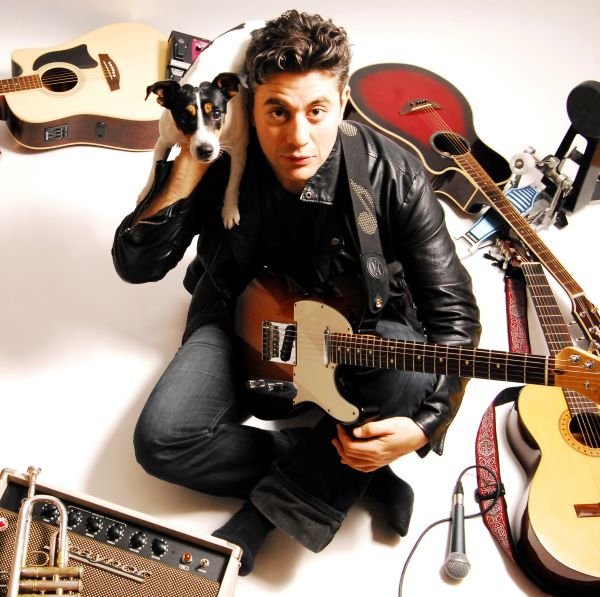 Sami Ghawi sitting on the floor with a dog surrounded by guitars and an amp