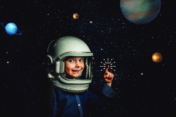 child wearing a astronaut helmet against a black background of stars and planet