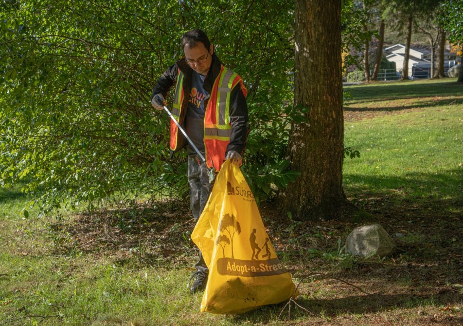  A person in a high-visibility vest is cleaning up with a bag, with a park backdrop.