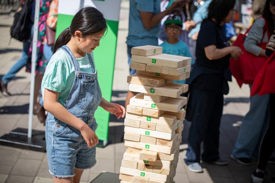 A young girl playing a giant game of Jenga at an outdoor community event.