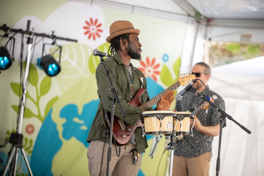 Musicians performing on stage with a floral backdrop, one playing guitar and the other on percussion.